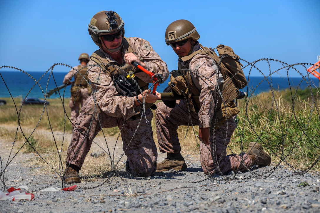 Two Marines kneel while cutting concertina wire.