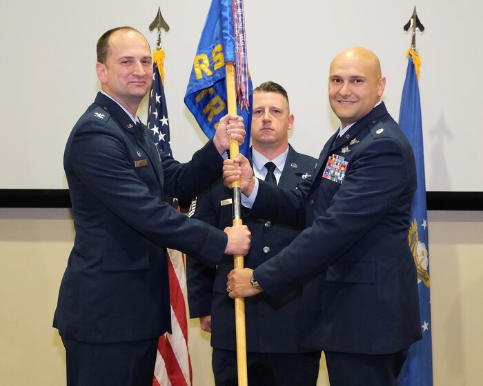 photo of three uniformed, US military members standing on a stage, two are holding a unit flag