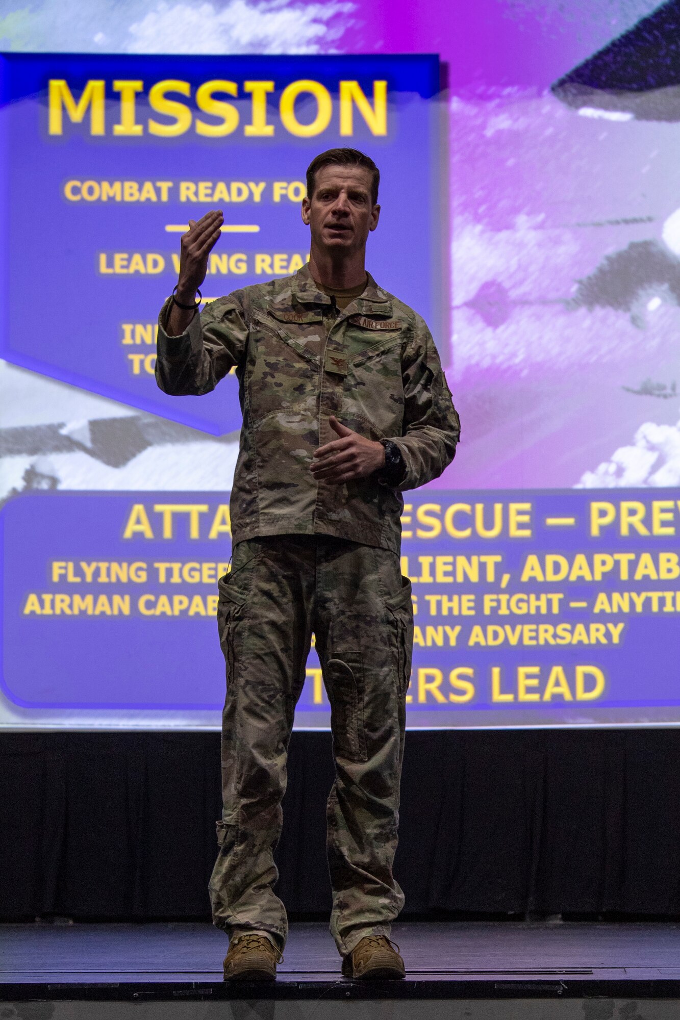 A photo of a man standing on a stage with a purple background on the projector.