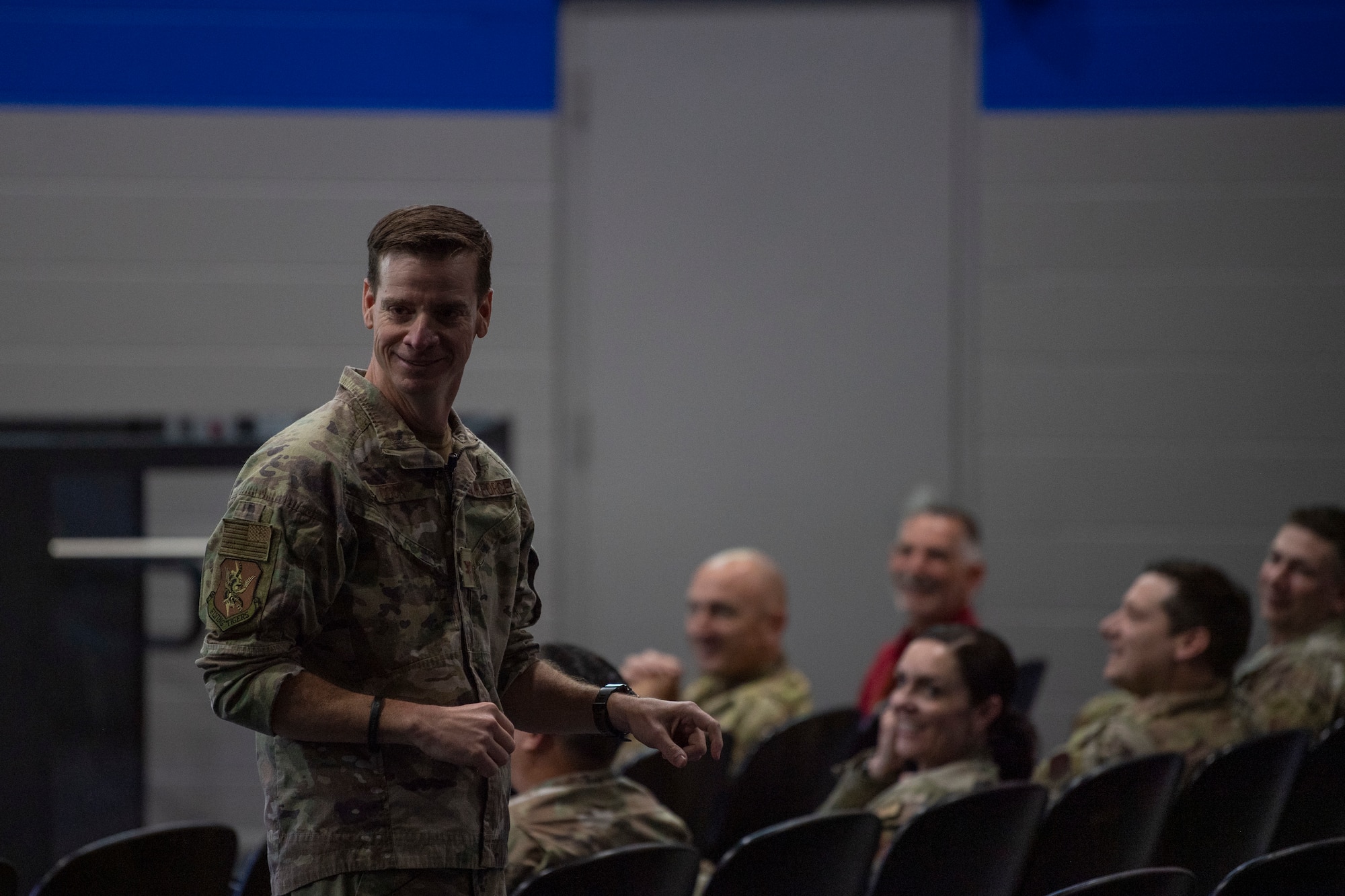 A photo of a man walking down an isle with people in the background sitting down in  theater seats.