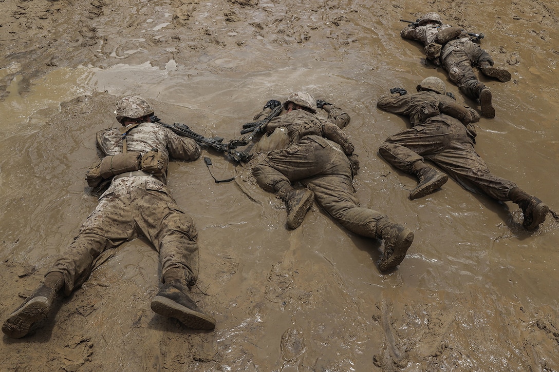Marine Corps recruits lay in mud with their weapons during training.