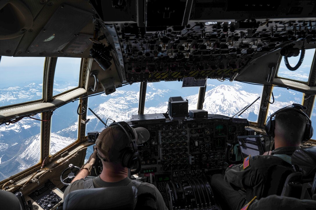 Airmen fly a military aircraft over snow-covered mountains.