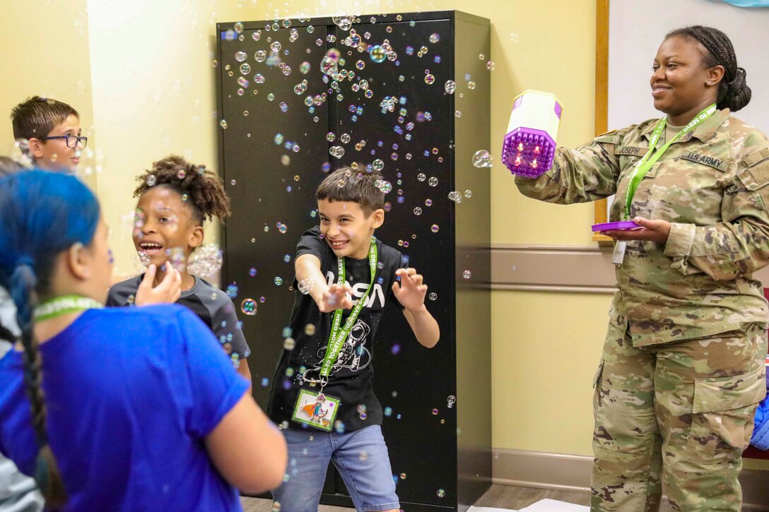 A soldier uses a toy to blow bubbles around children.