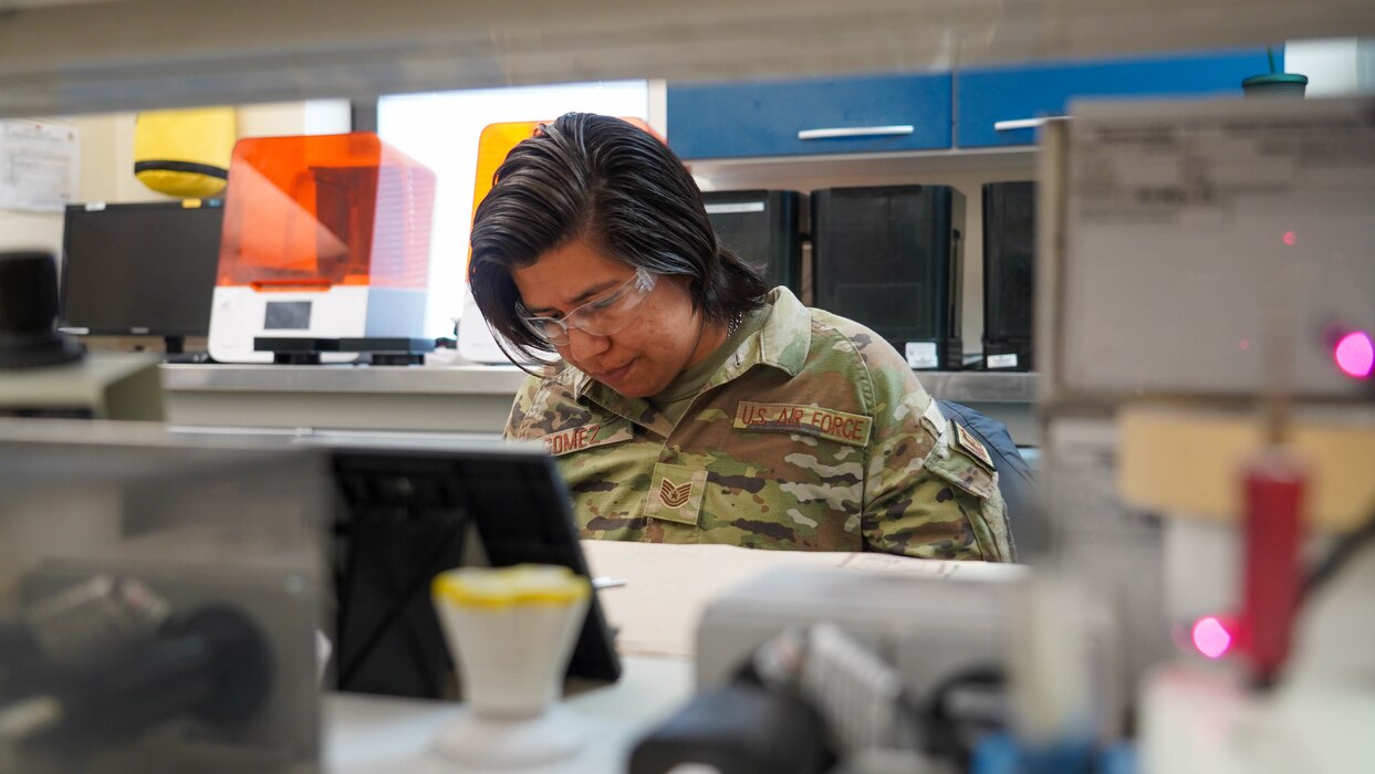 A woman sitting in the middle of the photo, from the shoulders up, behind lab equipment.