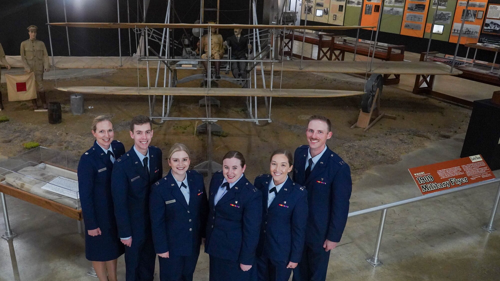 Six Airmen in uniform pose in front of a museum plane display.