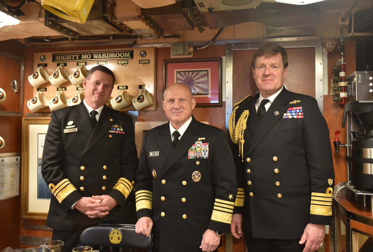 Three men in uniform pose for a photograph aboard a submarine.