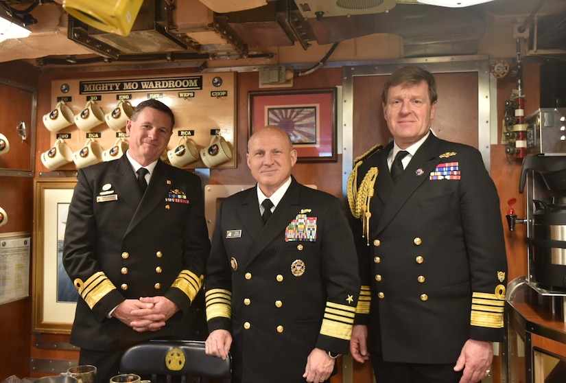 Three men in uniform pose for a photograph aboard a submarine.