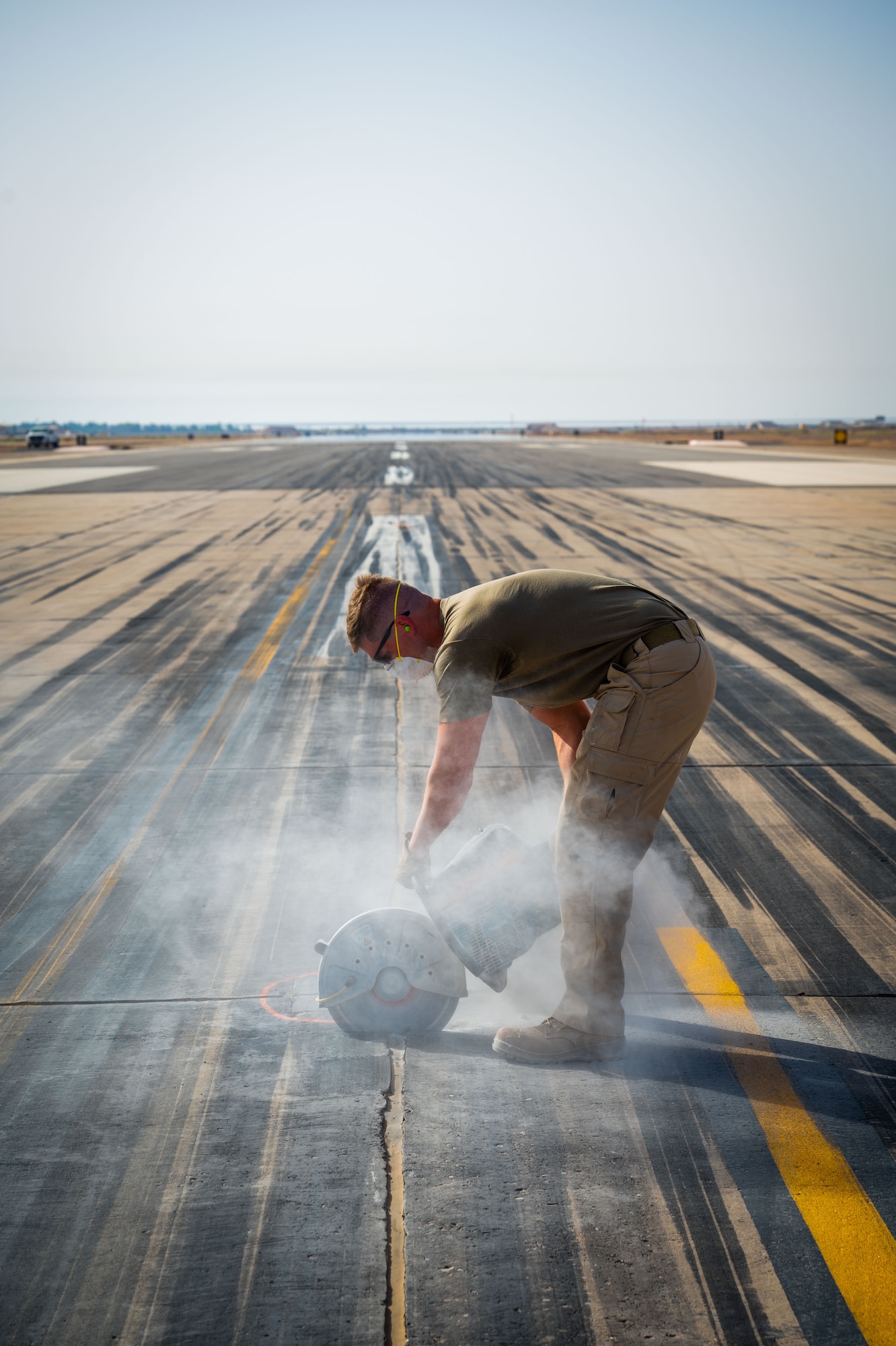 A man operates a concrete saw on a runway.