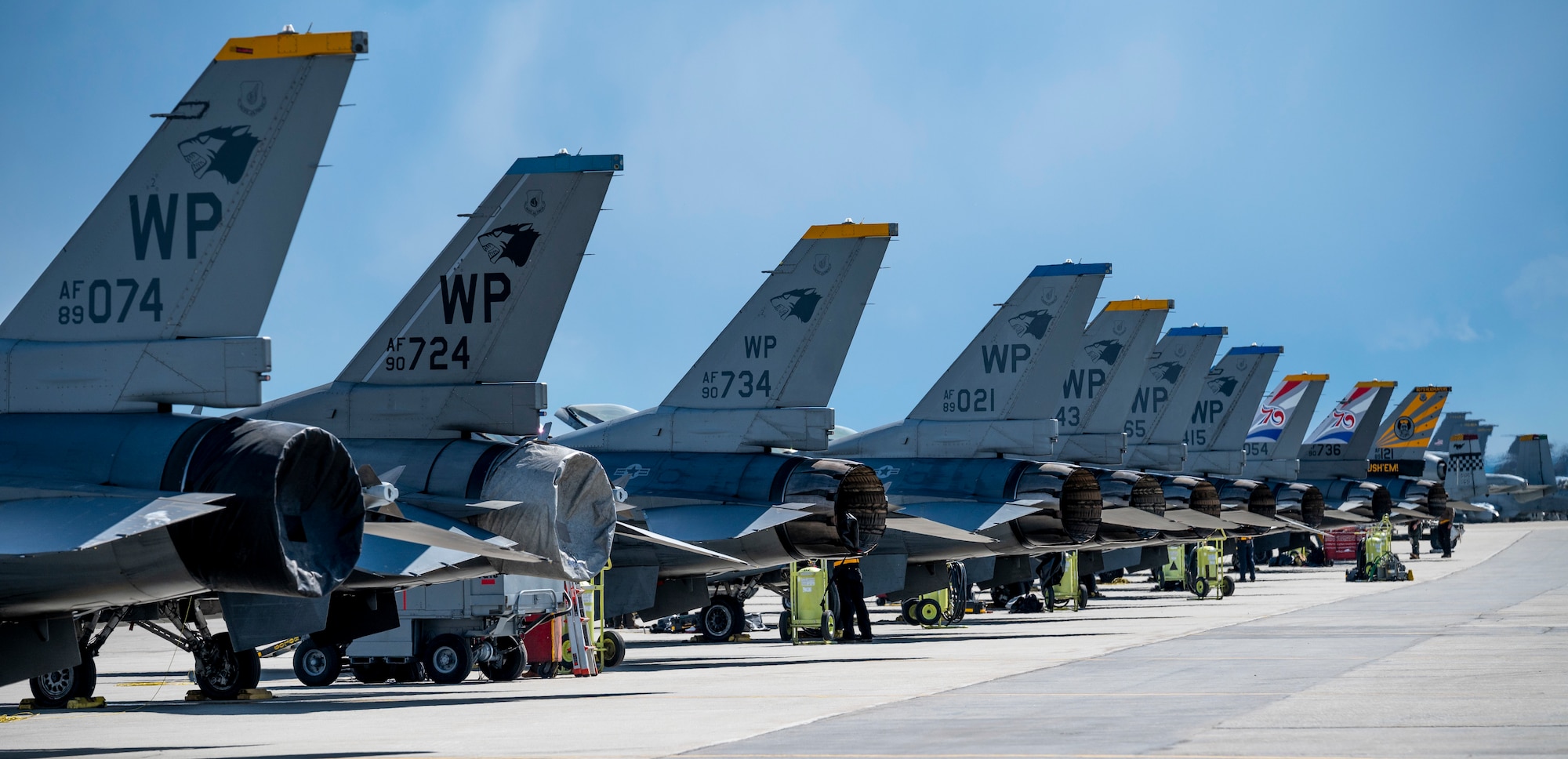 Kunsan AB F-16 Fighting Falcons are parked in line on the flight line and image captures their tail art