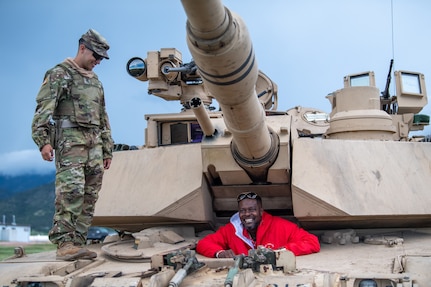 Two people, one in uniform and one in civilian clothes, pose with a tank.