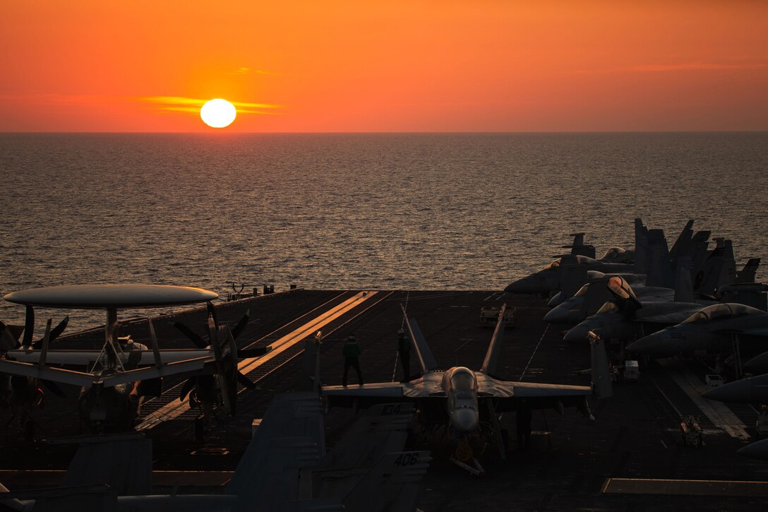 Planes sit on the deck of a ship at twilight.