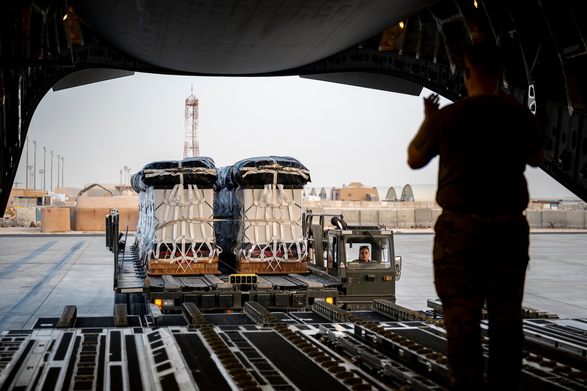 Military members in uniform transport cargo towards the back of an aircraft.