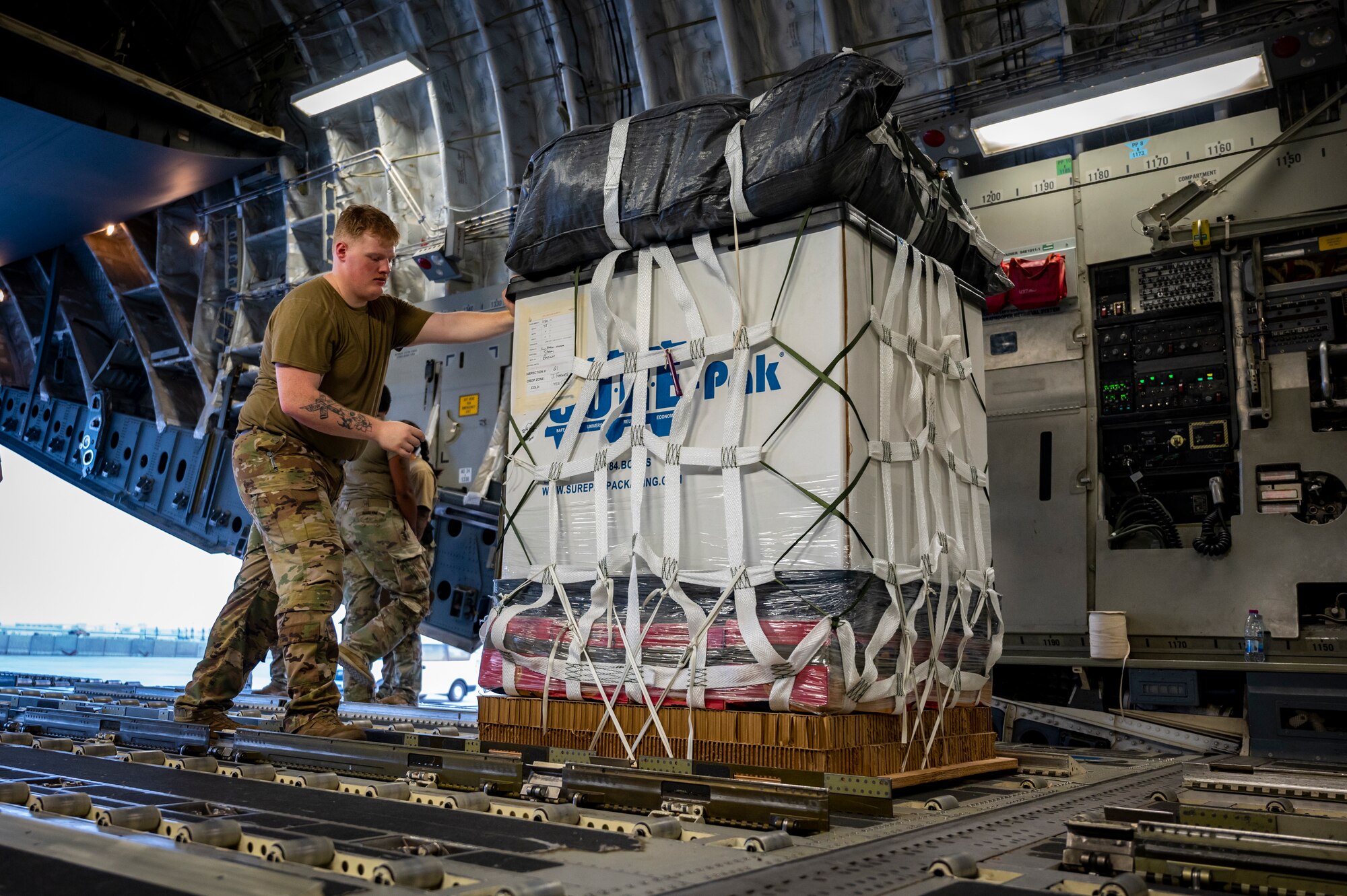 A military member in uniform moves cargo into the back of an aircraft.