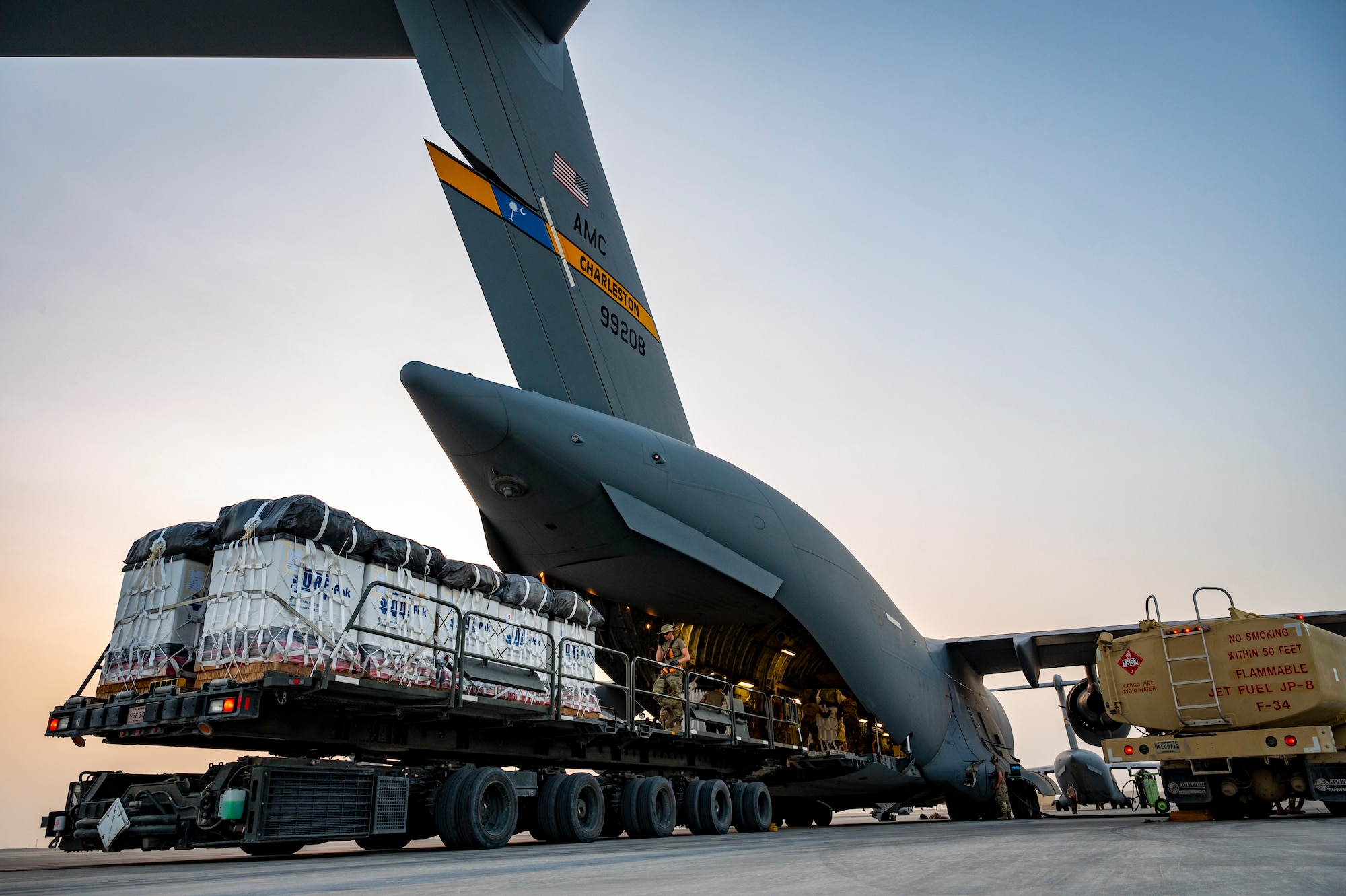 Military members in uniform move cargo into the back of an aircraft.