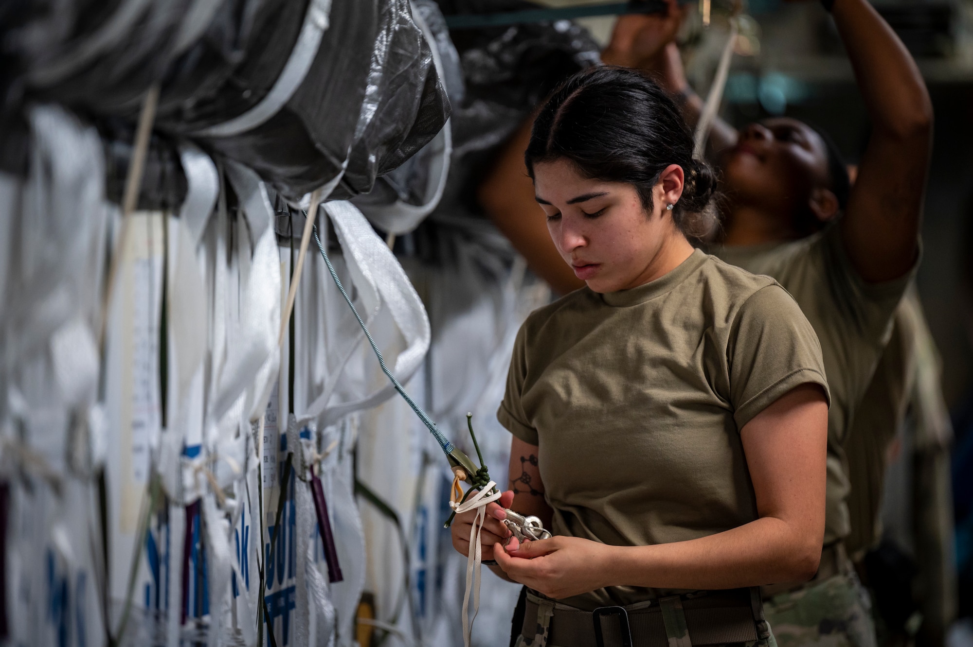 A military member in uniform ties down cargo on the bed of an aircraft.
