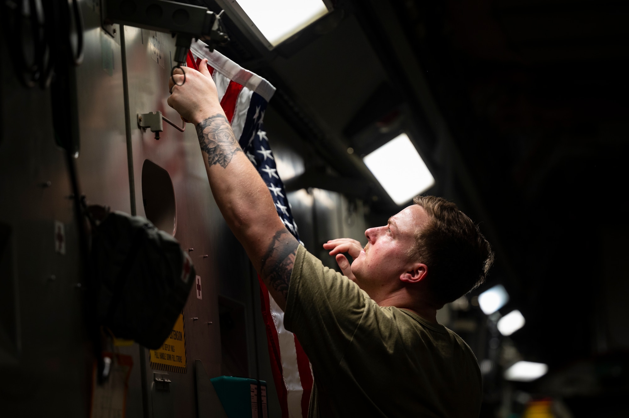 A military member in uniform hangs an American flag on the wall of a C-17.