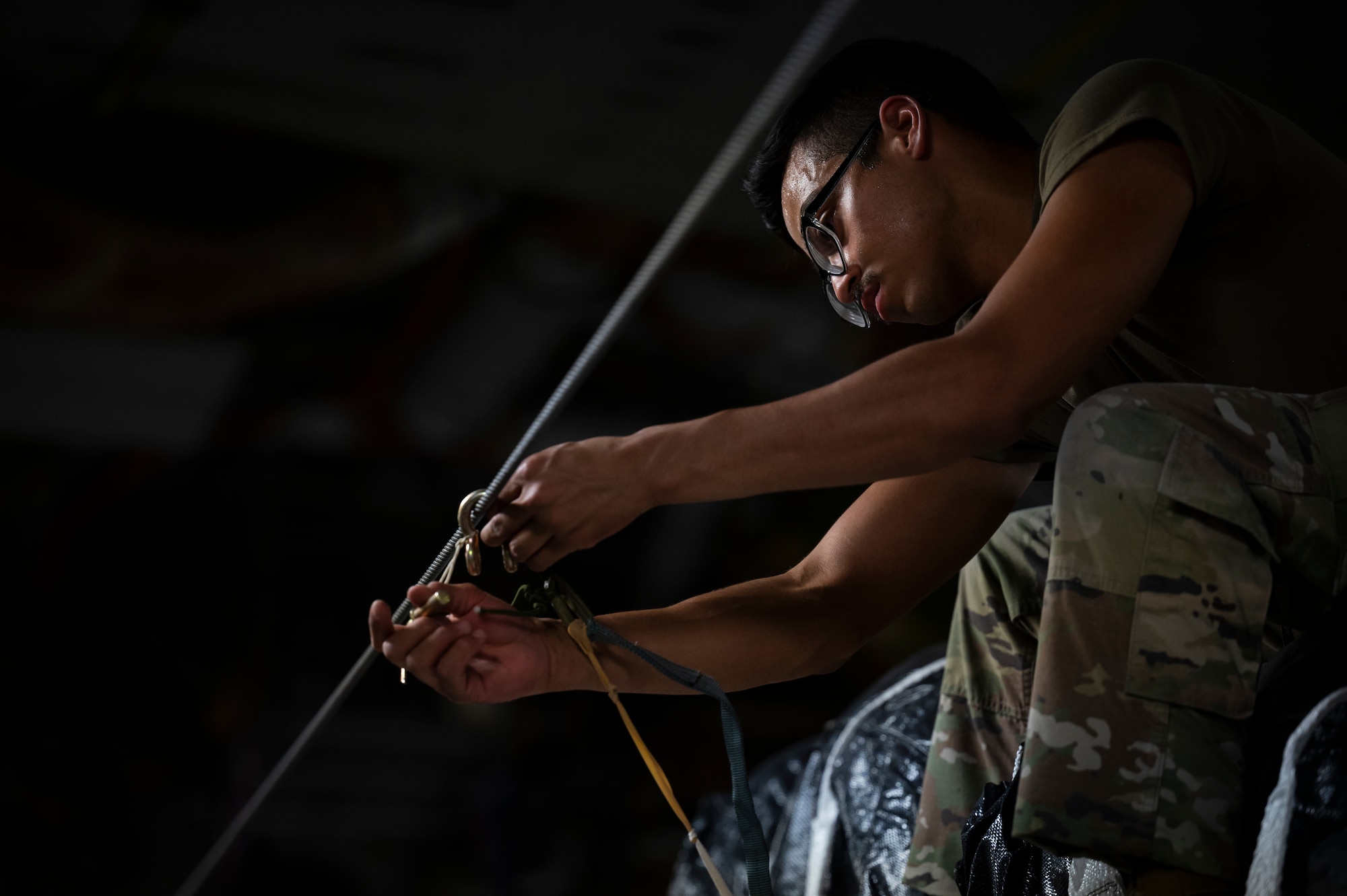 A military member in uniform ties cargo to a line.
