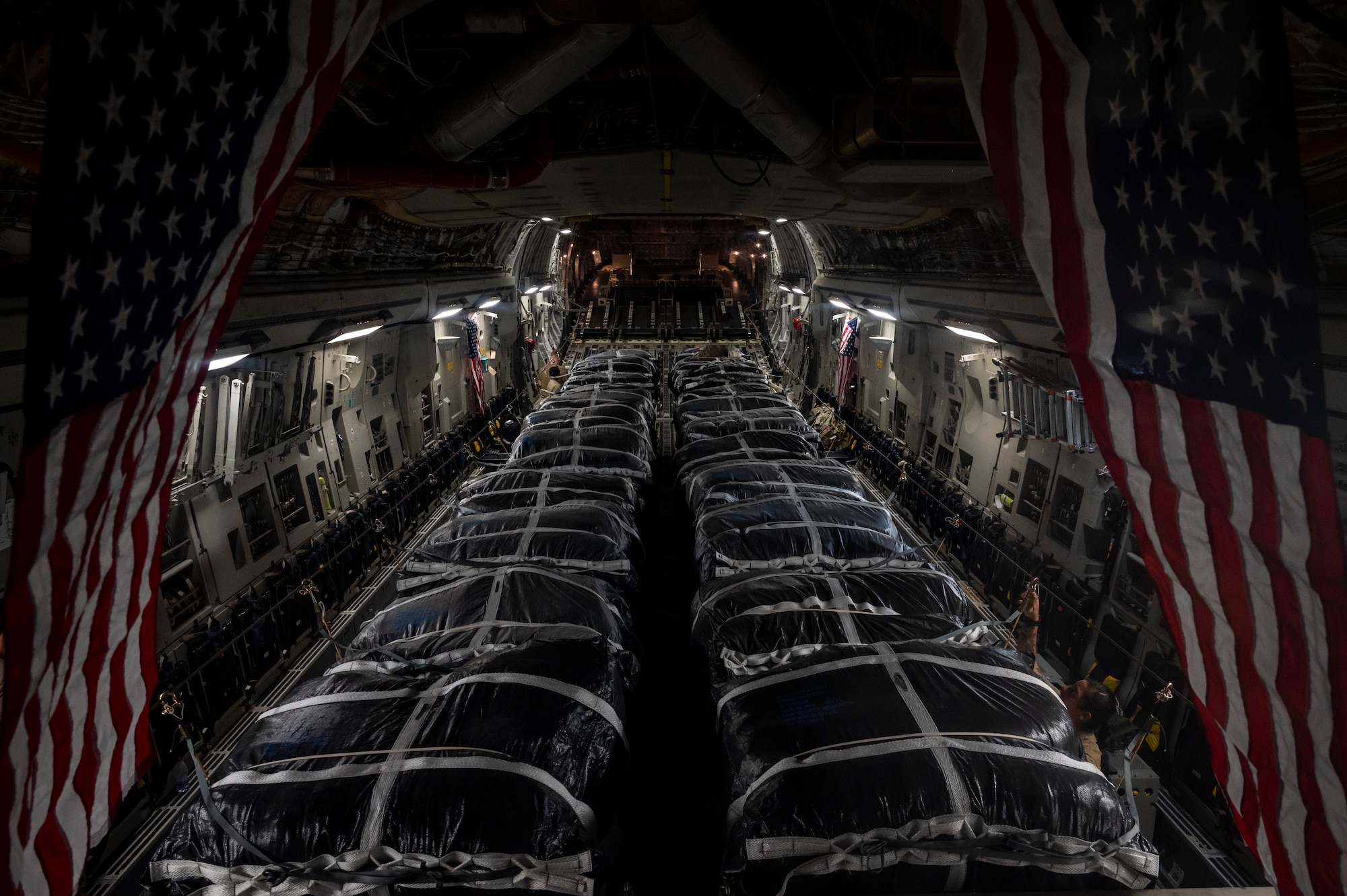 Military members in uniform tie down cargo on a plane