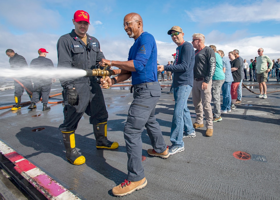 Sailors help embarked family and friends handle a firehose during a damage control rodeo aboard USS Nimitz (CVN 68).