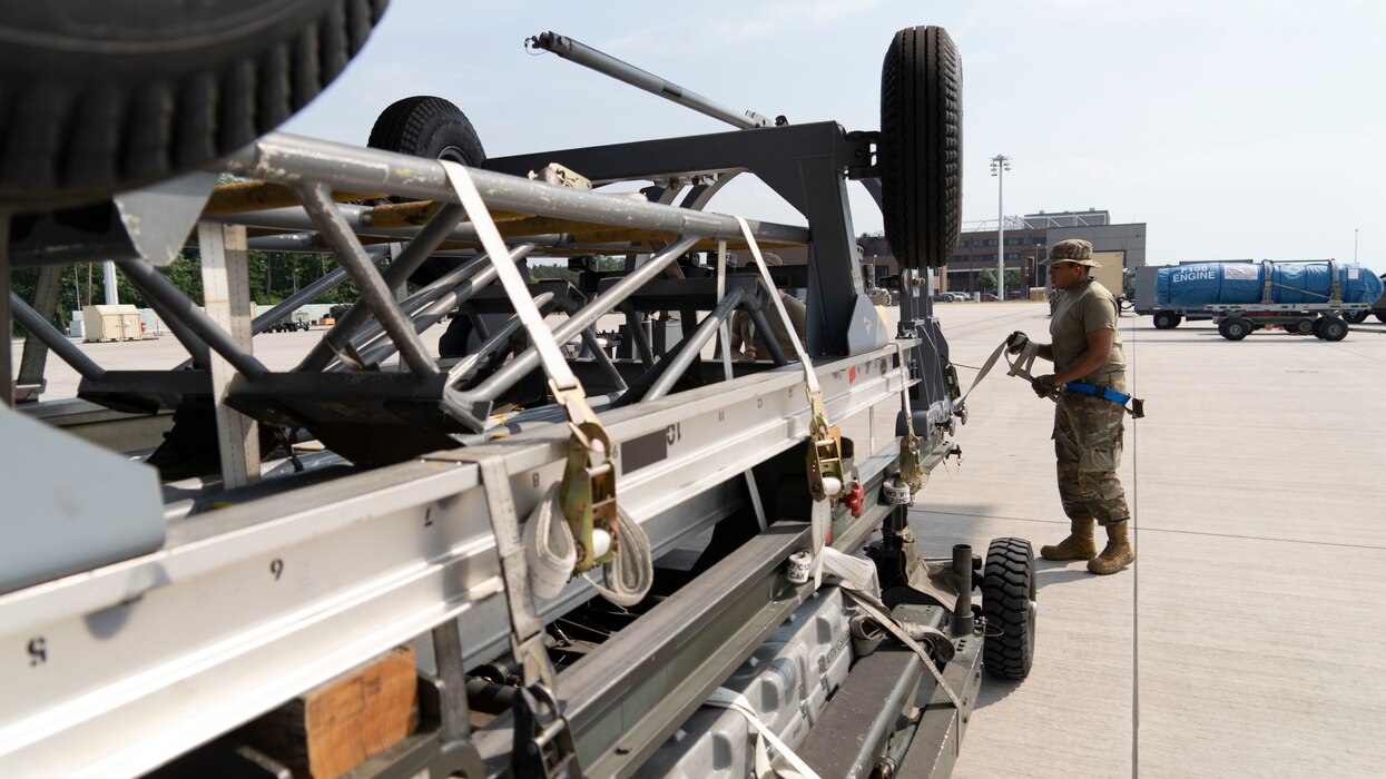 A photograph of a U.S. Air Force Airman loading cargo into a military C-17. The photograph is a side view with a natural leading line using the cargo to lead the viewer to the Airman at the end of the photo, who is holding a strap securing the cargo.