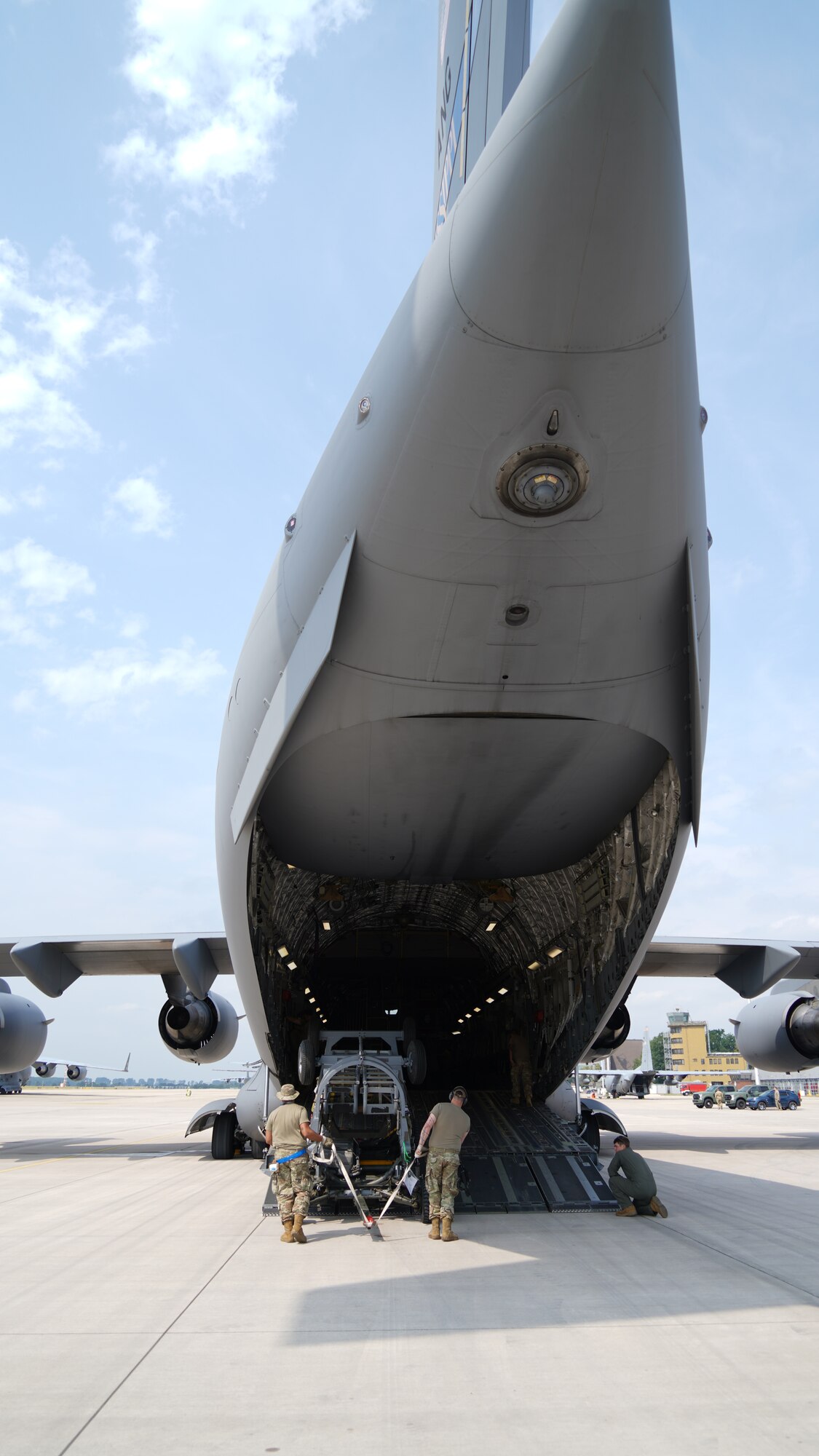 Two U.S. Air Force Airmen load cargo into the back of an open C-17 military aircraft.