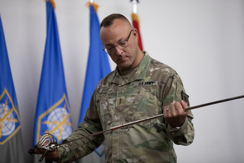 Chief Warrant Officer 5 William Davis holds a saber, looking at it closely.