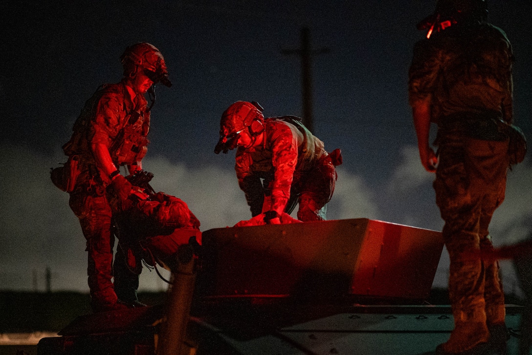 Three sailors work atop a Humvee at night, illuminated by a red light.