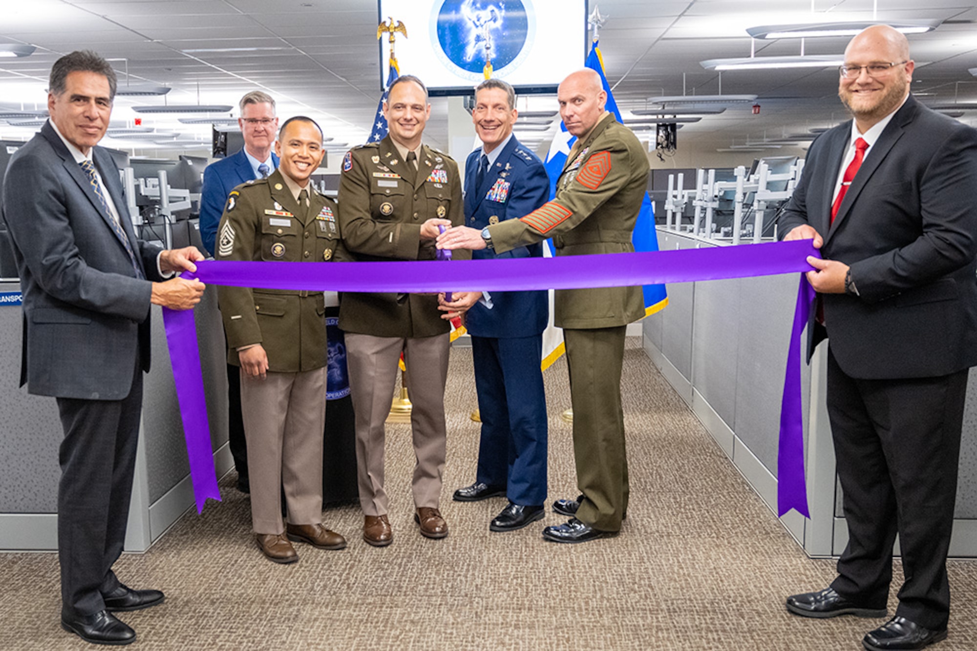 people standing in the hall of a cubical-type office holding a purple ribbon.