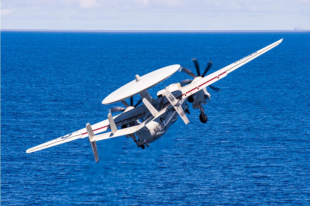 An aircraft flies at an angle above a body of water.