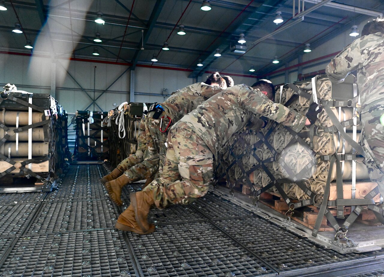People in uniform push a pallet into position aboard a military cargo plane.