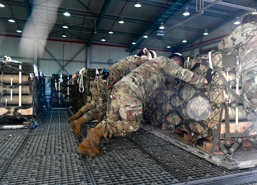 People in uniform push a pallet into position aboard a military cargo plane.