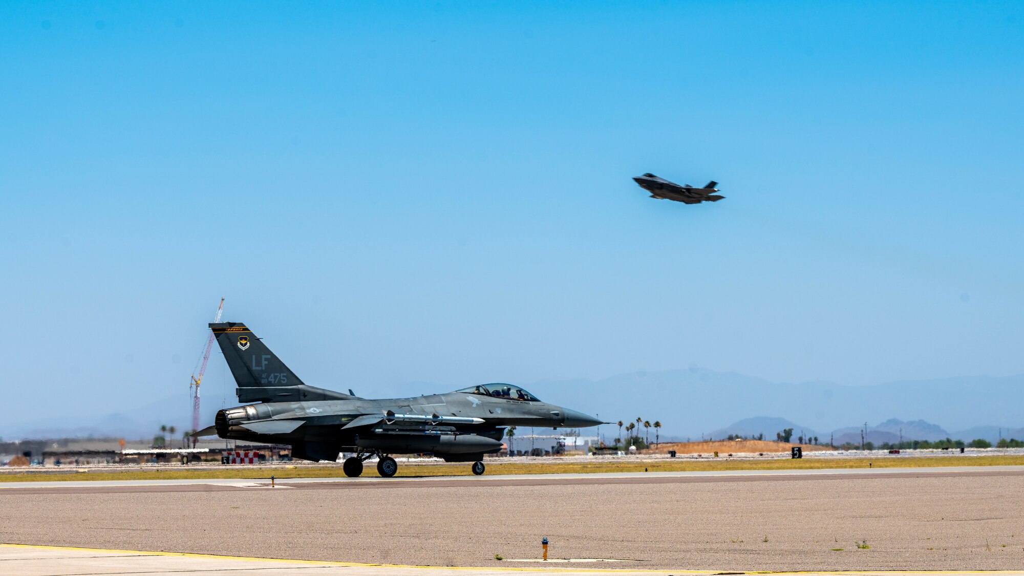 An F-16 Fighting Falcon assigned to the 56th Fighter Wing, taxis on the flightline while an F-35 Lightning II takes off overhead at Luke Air Force Base, Arizona June 23, 2023.