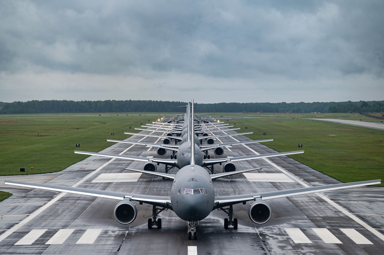 Several aircraft stage in line on a runway.