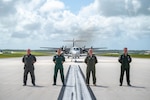 Four Airmen standing together in front of an aircraft on a landing strip