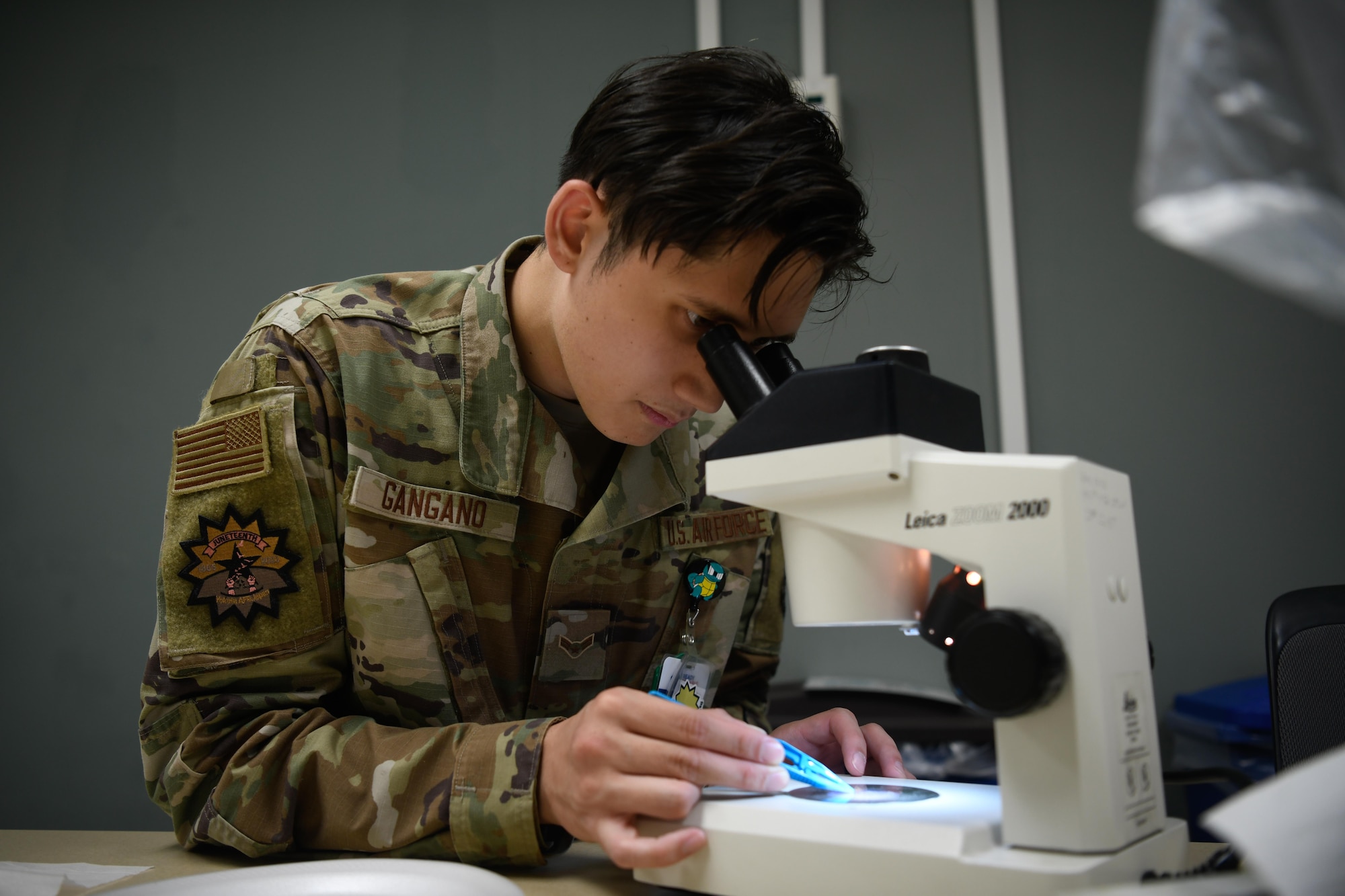 A service member looks under a microscope.