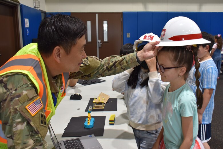 Maj. Hyung Oh, Exercise and Plans Officer at the U.S. Army Corps of Engineers – Far East District, places a hard hat on one of the students during a STEM event hosted by USACE at West Elementary School on Camp Humphreys, South Korea, on May 30. Through hands-on activities, the team demonstrates how STEM is all around them in the world and encourages further interest in the field. (U.S. Army photo by Rachel Napolitan)