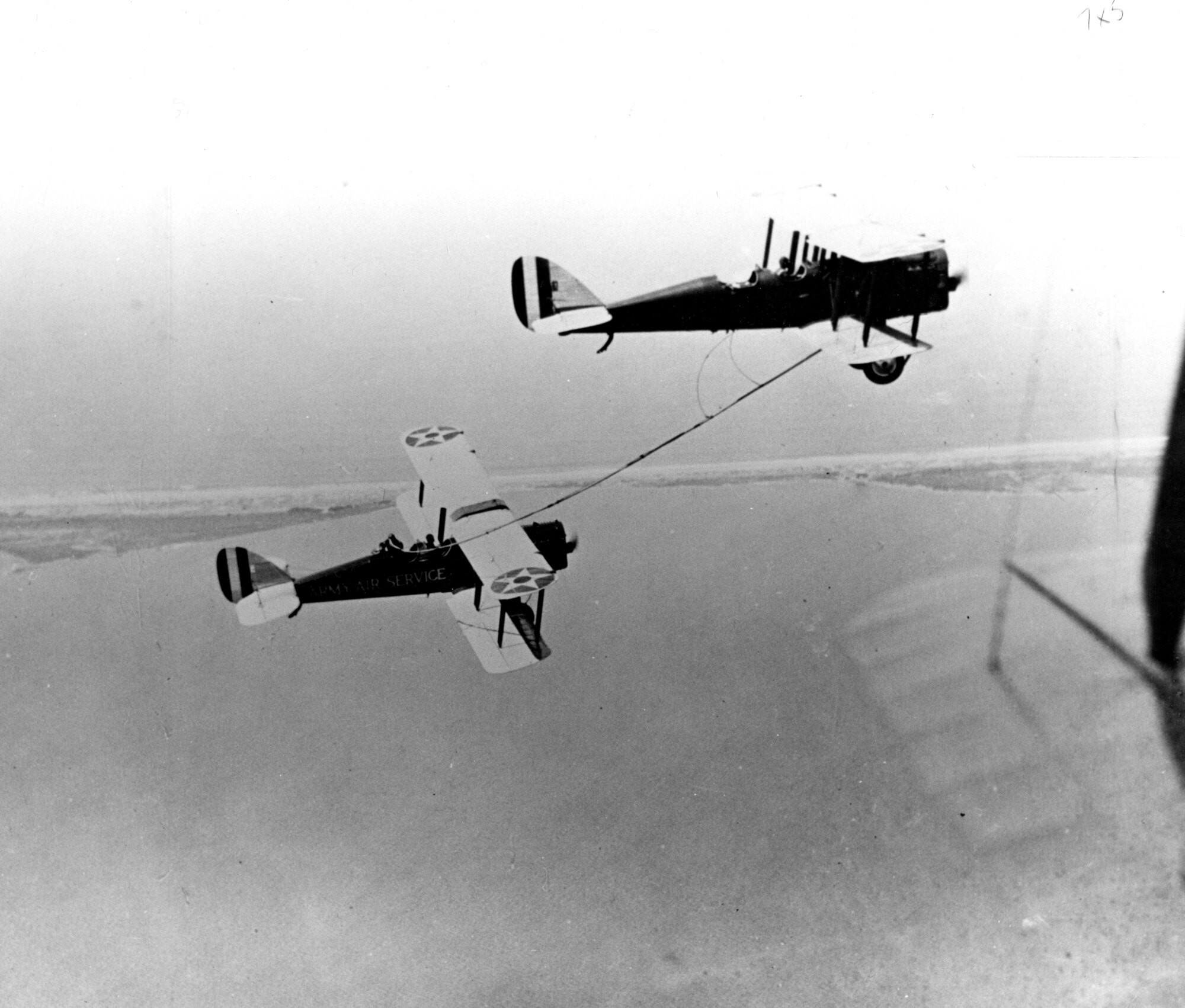 Two planes fly with a hose connecting them.