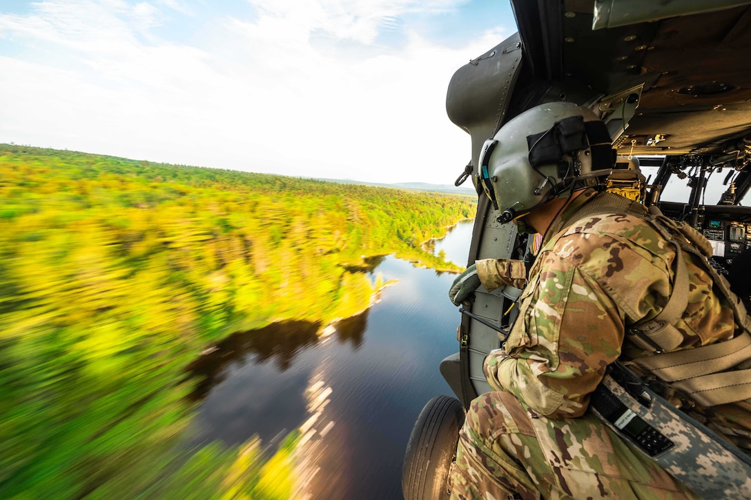 A soldier looks out on woods and water from a helicopter.