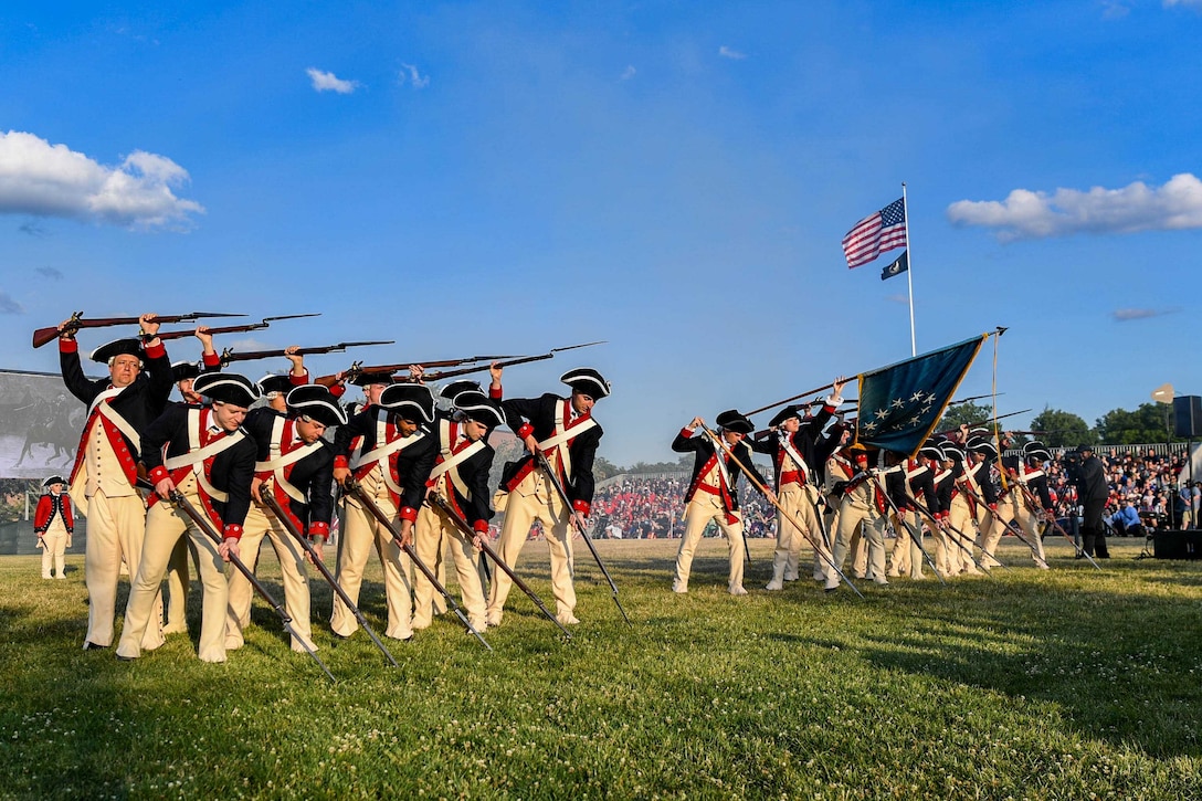 Soldiers in colonial uniforms and using colonial rifles perform in formation.
