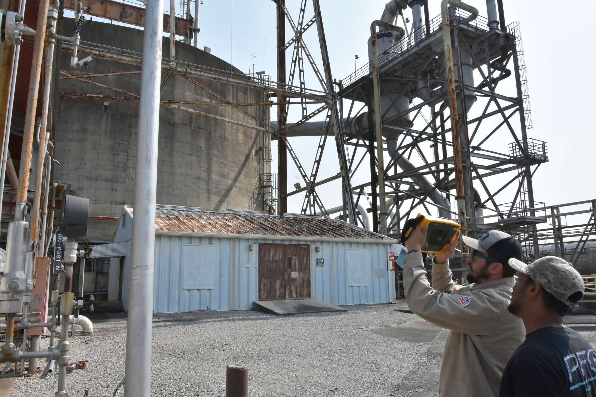 Wayne Horton, ultrasound lead at Arnold Air Force Base, Tenn., right, looks on as Robert Hastings, an electrician at Arnold AFB, uses a recently-acquired acoustic imager to check equipment near the J-4 test facility at Arnold for leaks May 26, 2023. The imager can identify leaks in compressed air, gas and vacuum systems, and allows users to see the exact location of a leak on a digital image displayed on the device. It can also determine the distance, size and decibel level of a leak. The imager was one of seven projects that received funding through the 2023 AEDC Spark Tank program, which allows members of the AEDC workforce to propose suggestions for improving AEDC processes, products and test capabilities. (U.S. Air Force photo by Bradley Hicks) (This image was altered by obscuring a building number for security purposes.)