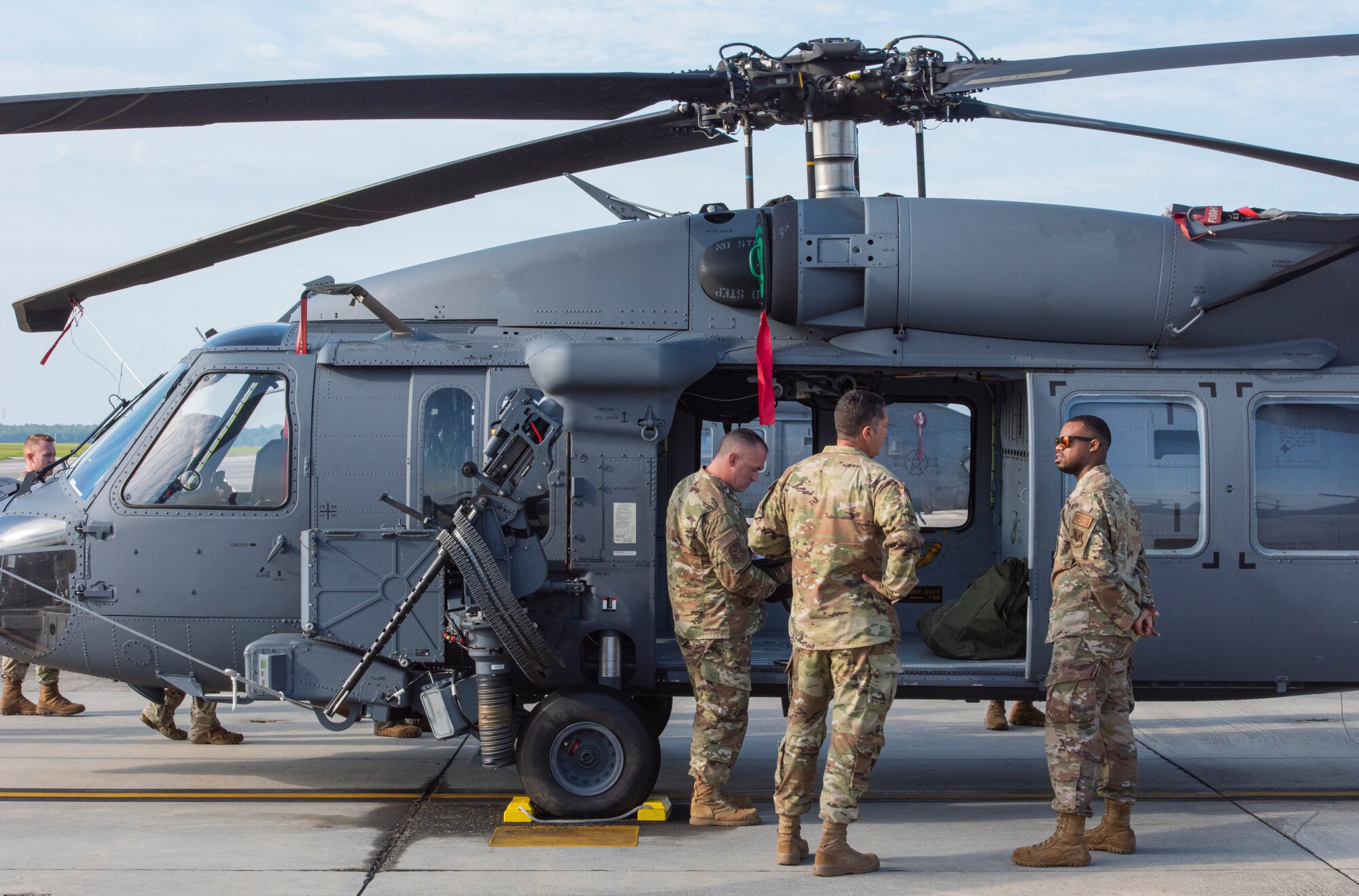 A photo of three people in military uniform standing on the left side of an HH60 Whiskey helicopter, talking.