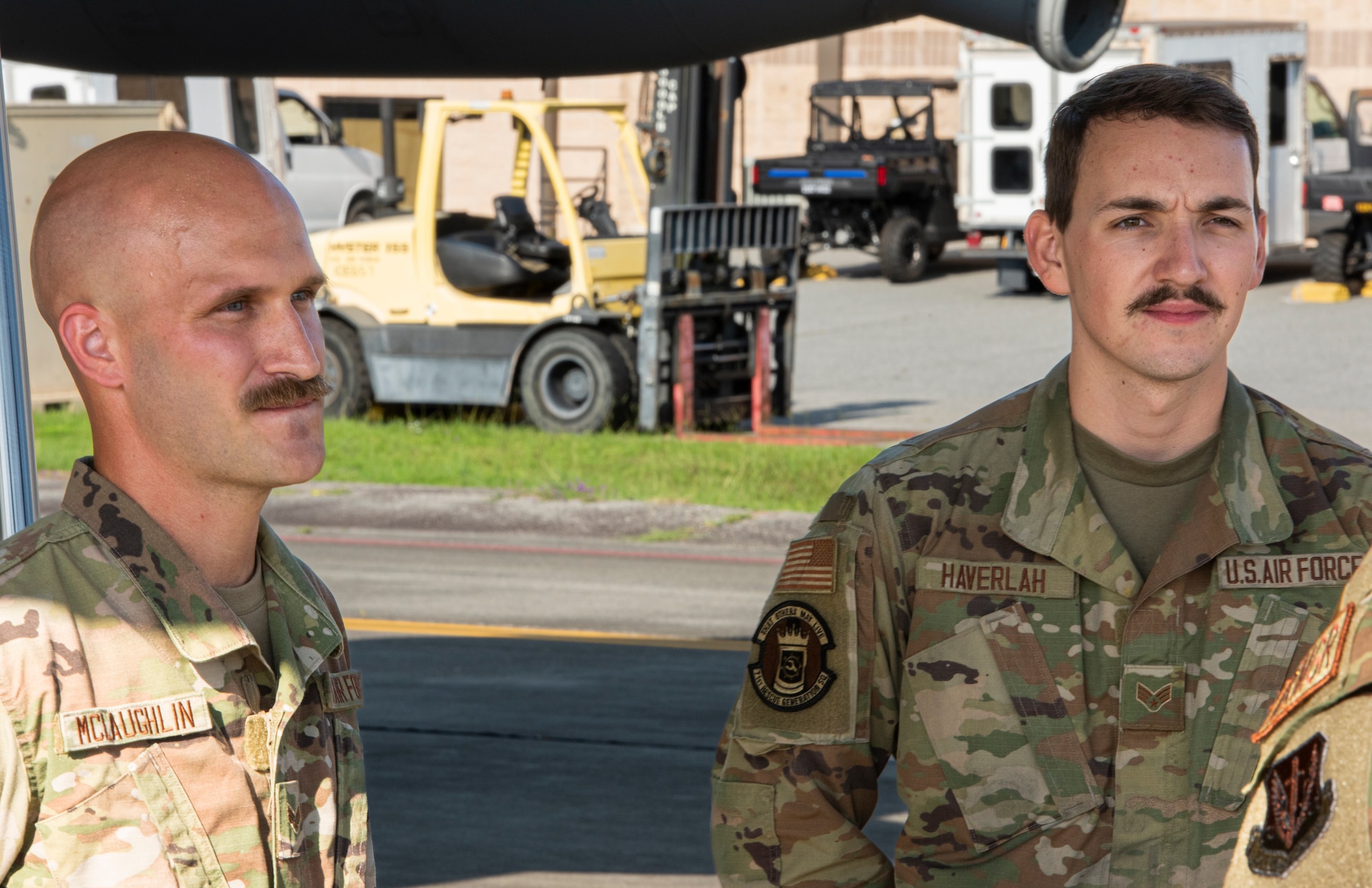 A photo of two people in military uniform, with a fork lift in the back ground.