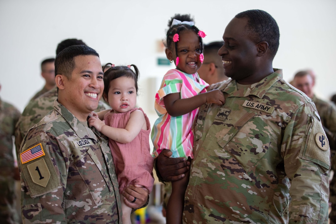 Smiling soldiers hold children during a deployment ceremony.