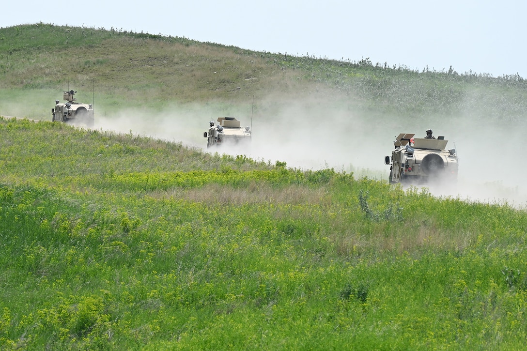 Military vehicles drive up a hill.