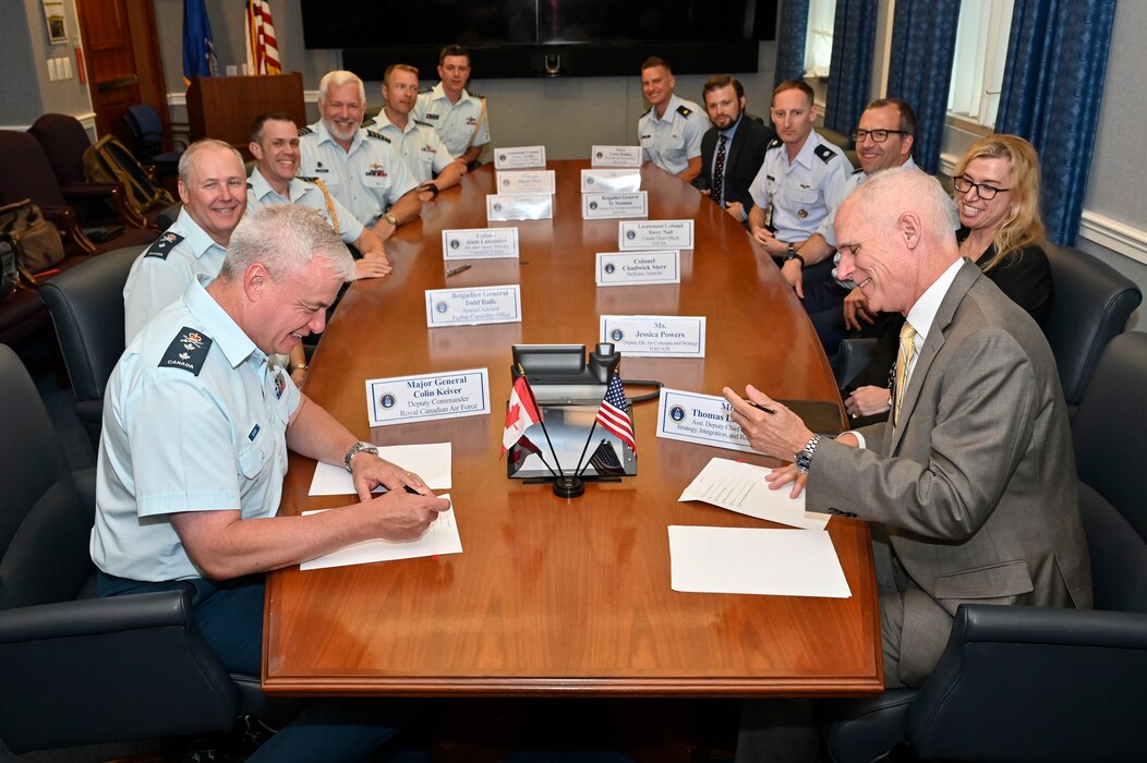 Royal Canadian Air Force Deputy Commander Maj. Gen. Colin Keiver and U.S. Air Force Assistant Deputy Chief of Staff, Strategy, Integration and Requirements Thomas Lawhead, sign a ‘Terms of Reference’ as other members of the Bilateral American Canadian Optimization Network, or BACON, look on. The Terms of Reference set the roadmap for combined effort and solidifying the BACON forum through 2028. (U.S. Air Force photo by Eric Dietrich)