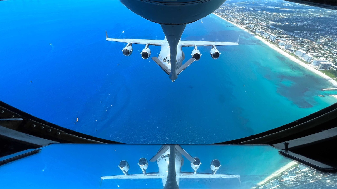 A large aircraft is reflected in a window over water.