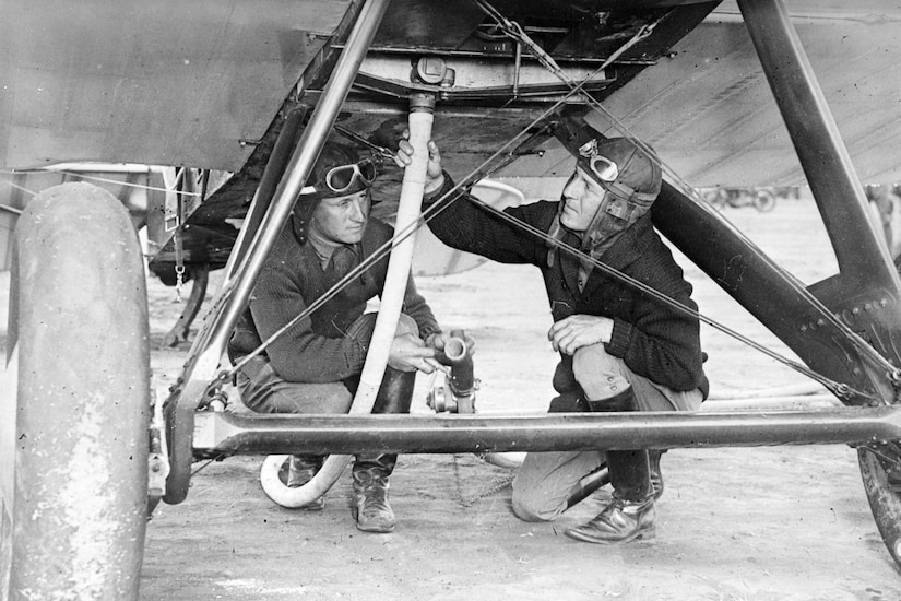 Two men stand underneath a plane.