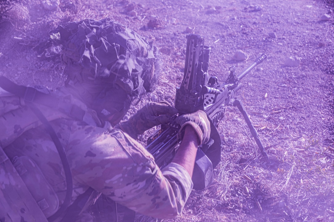 A soldier loads a weapon while kneeling on the ground covered by a purple haze.