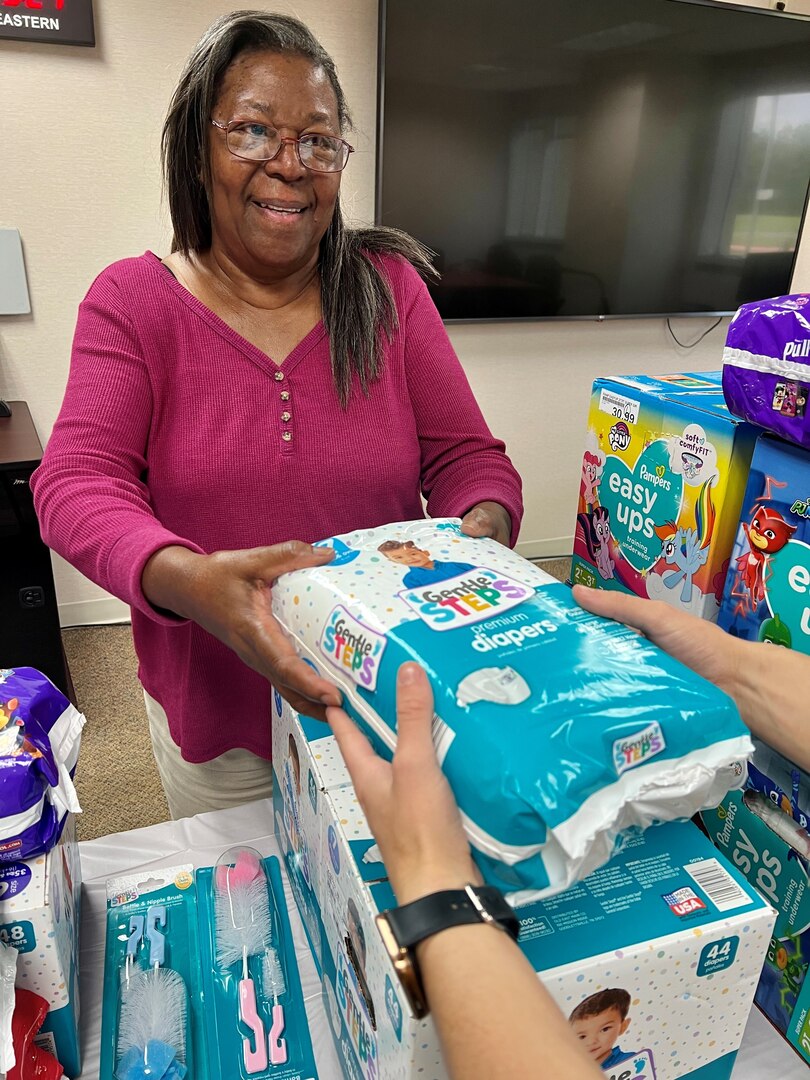 Woman handing pack of diapers over a tabletop display.