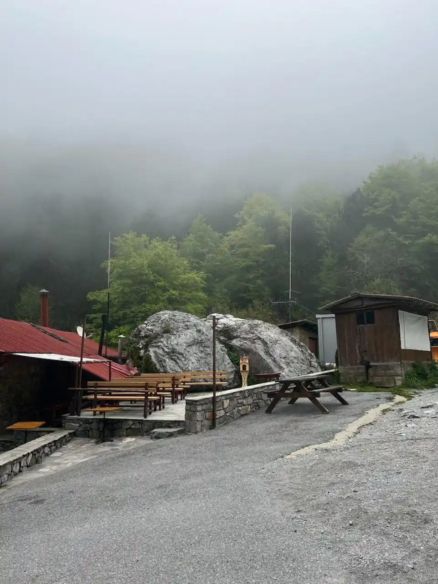Picnic tables sit behind the refuge building while clouds descend over trees and a large boulder.